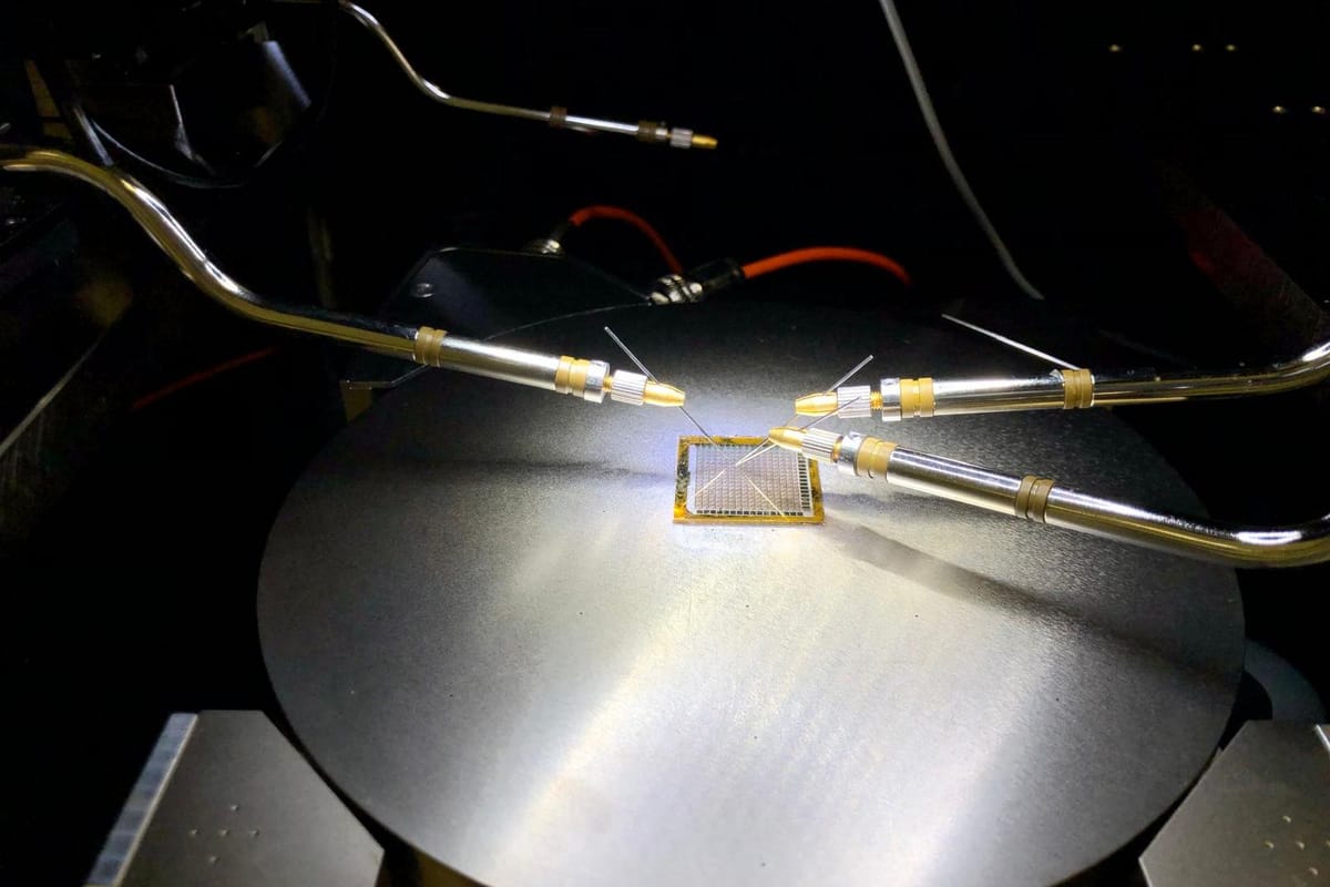 Gold-tipped probe needles landed on a die held on a metal chuck under directional light.